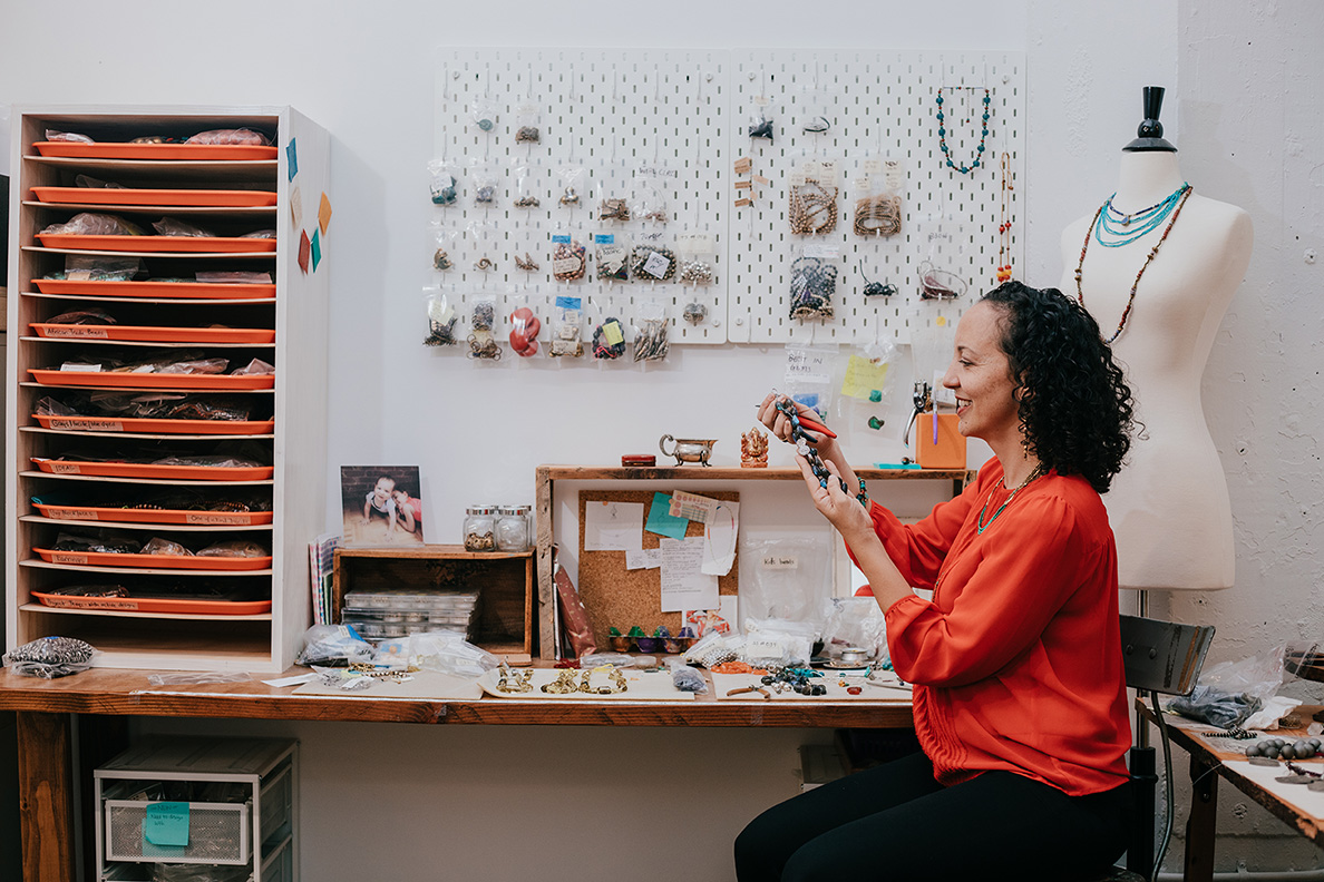 A woman crafts jewelry in a workspace.