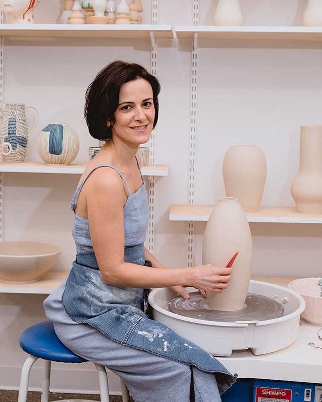 A woman smiles at the camera while creating pottery.