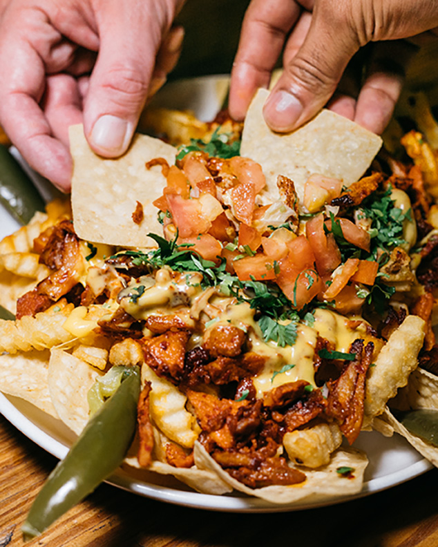 Hands grab chips out of a plate of nachos.