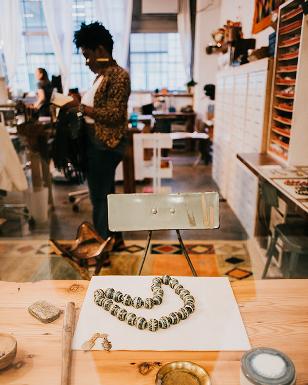 A necklace is on a workspace as people are in the background.
