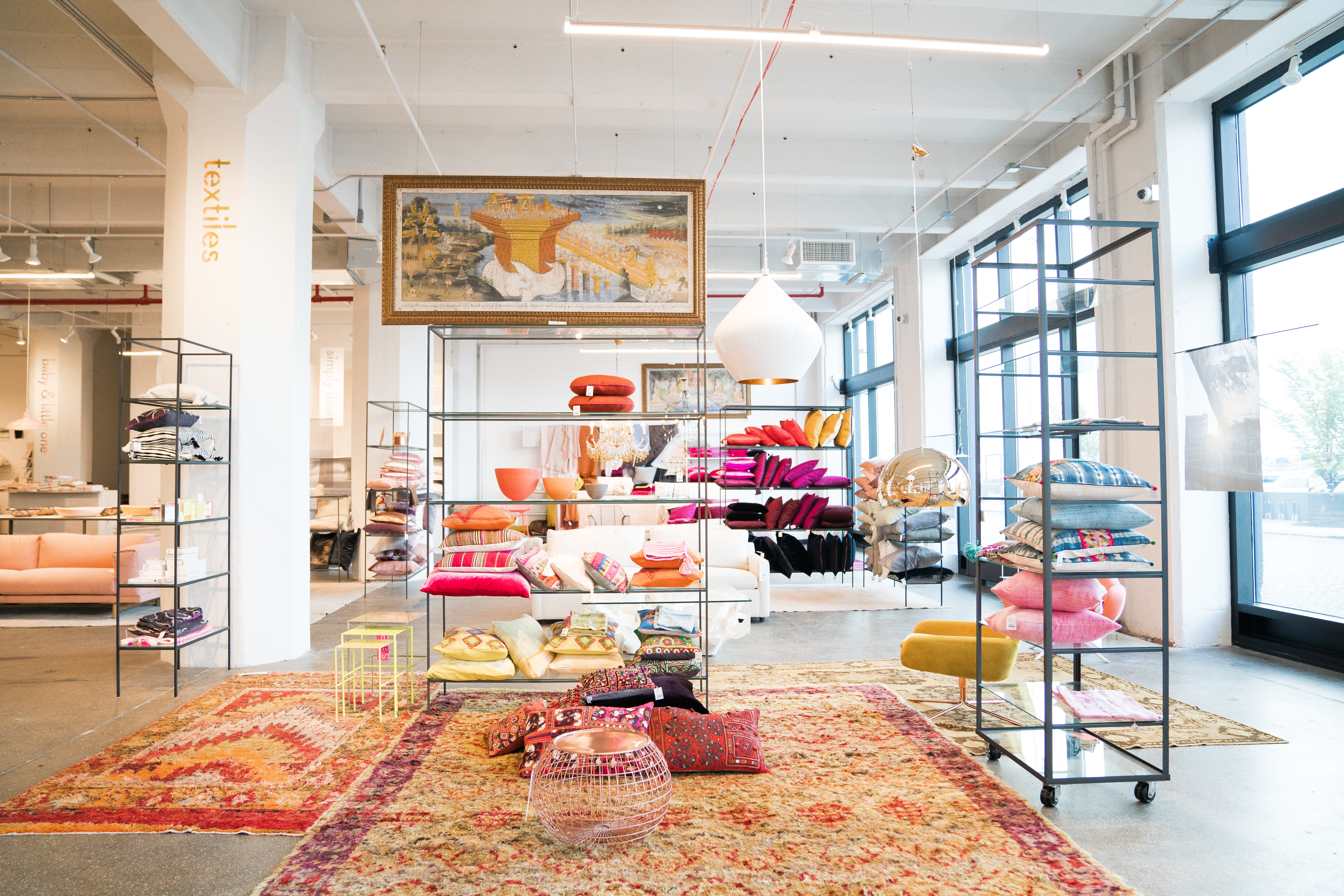 Pillows are on shelves and rugs are on the ground in a shop.