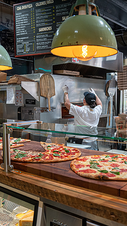A pizza store counter. Pizzas are displayed in front.