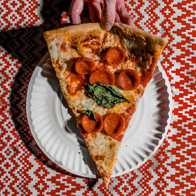 A hand holds a slice of pizza over a paper plate.