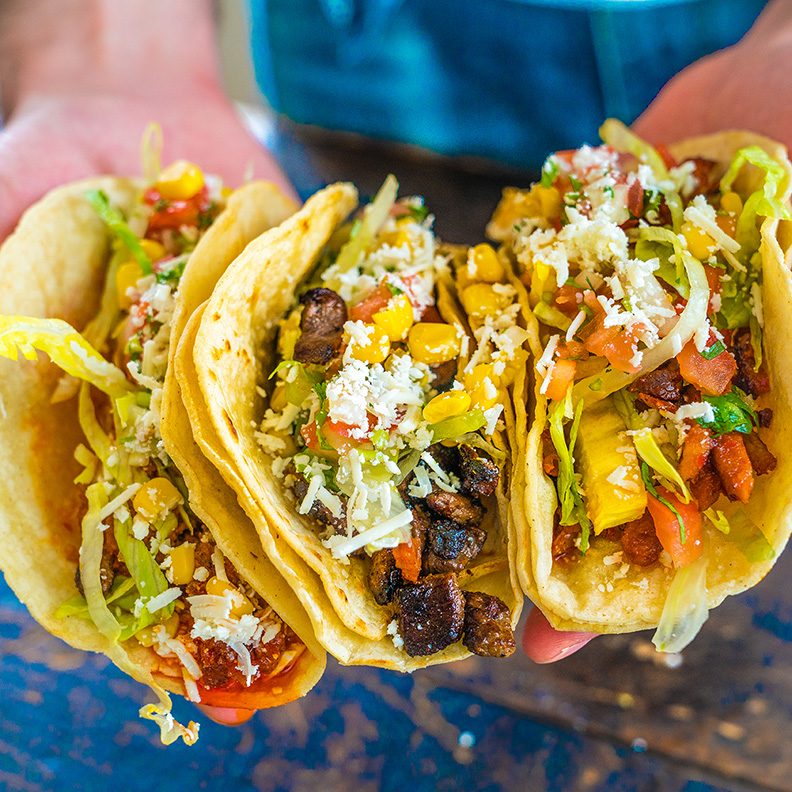 A person holds three tacos.