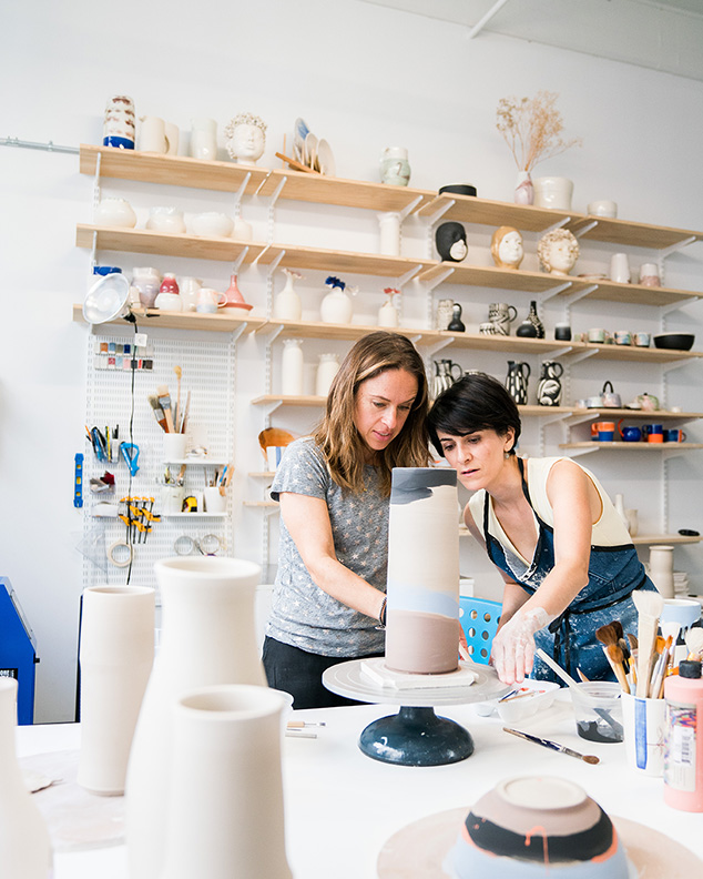 Two women work on a piece of pottery in a ceramics shop.