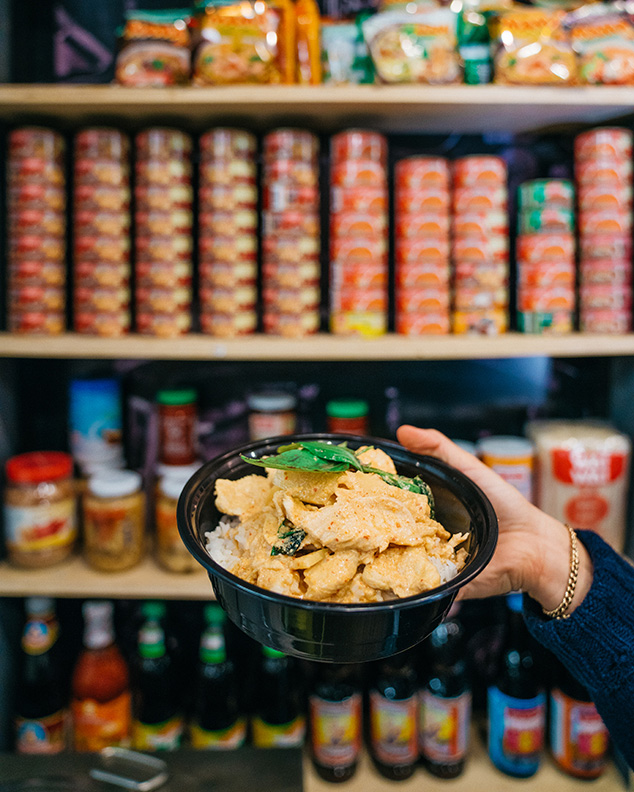 A hand holds a bowl of food in front of shelves of food.