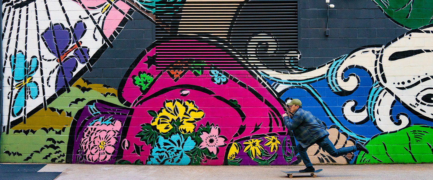 A person skateboards in front of a mural
