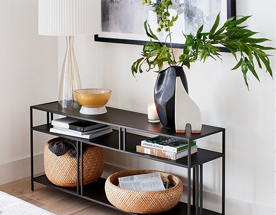 A black entryway table with baskets, vases, and other objects.