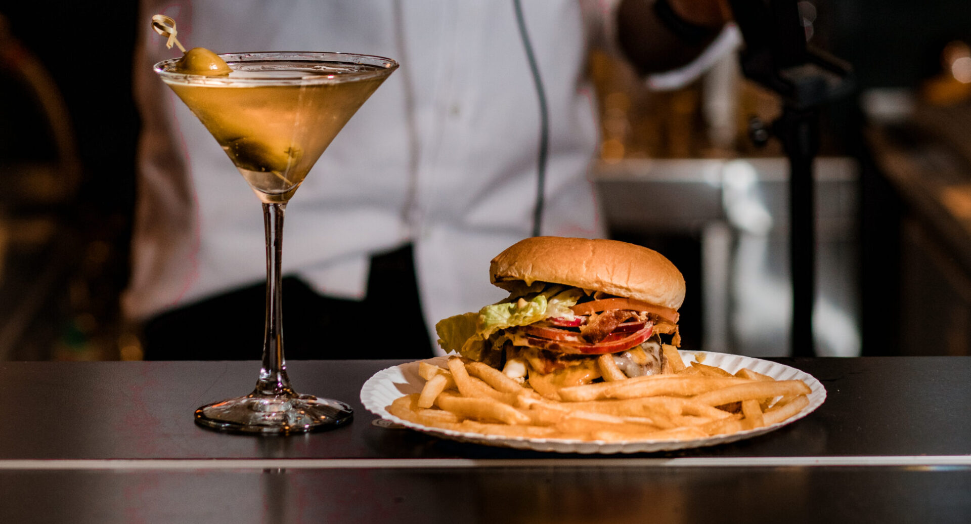 There is a burger and fries on a plate with a martini next to the food.