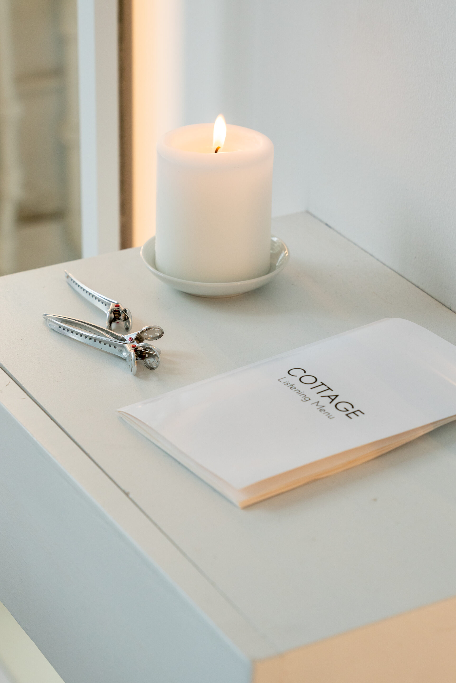 There is a table with a candle, hair tools, and a booklet for "Cottage," a hair salon.