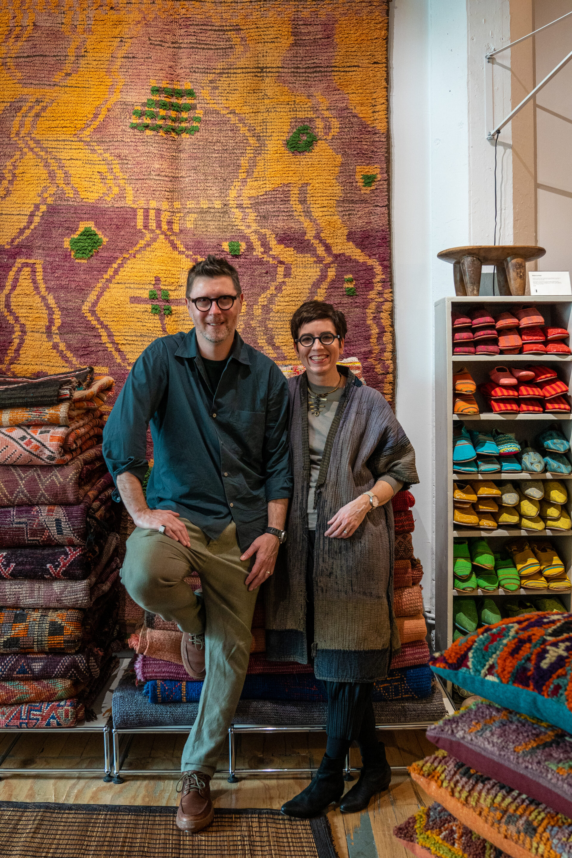 Two people are posing for a picture in front of rugs.