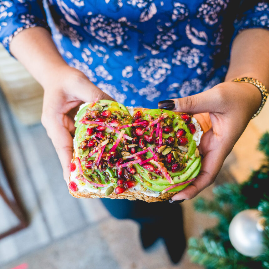 Someone is holding a piece of toast with avocado on it.