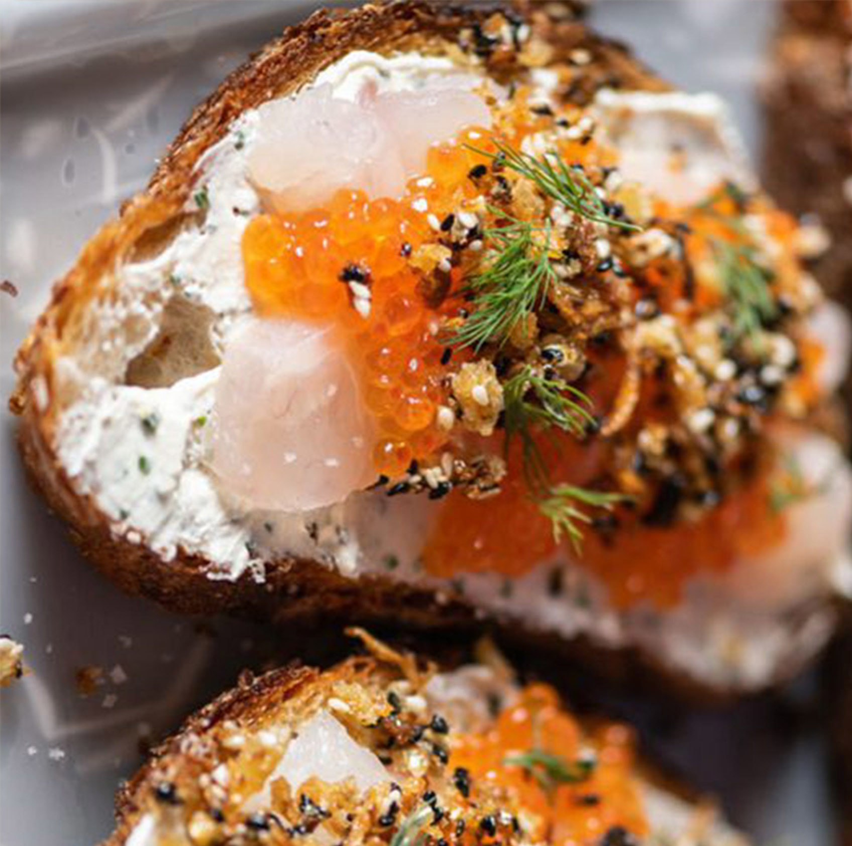 A piece of toast with cream cheese, fish, roe, herbs, and seasonings.