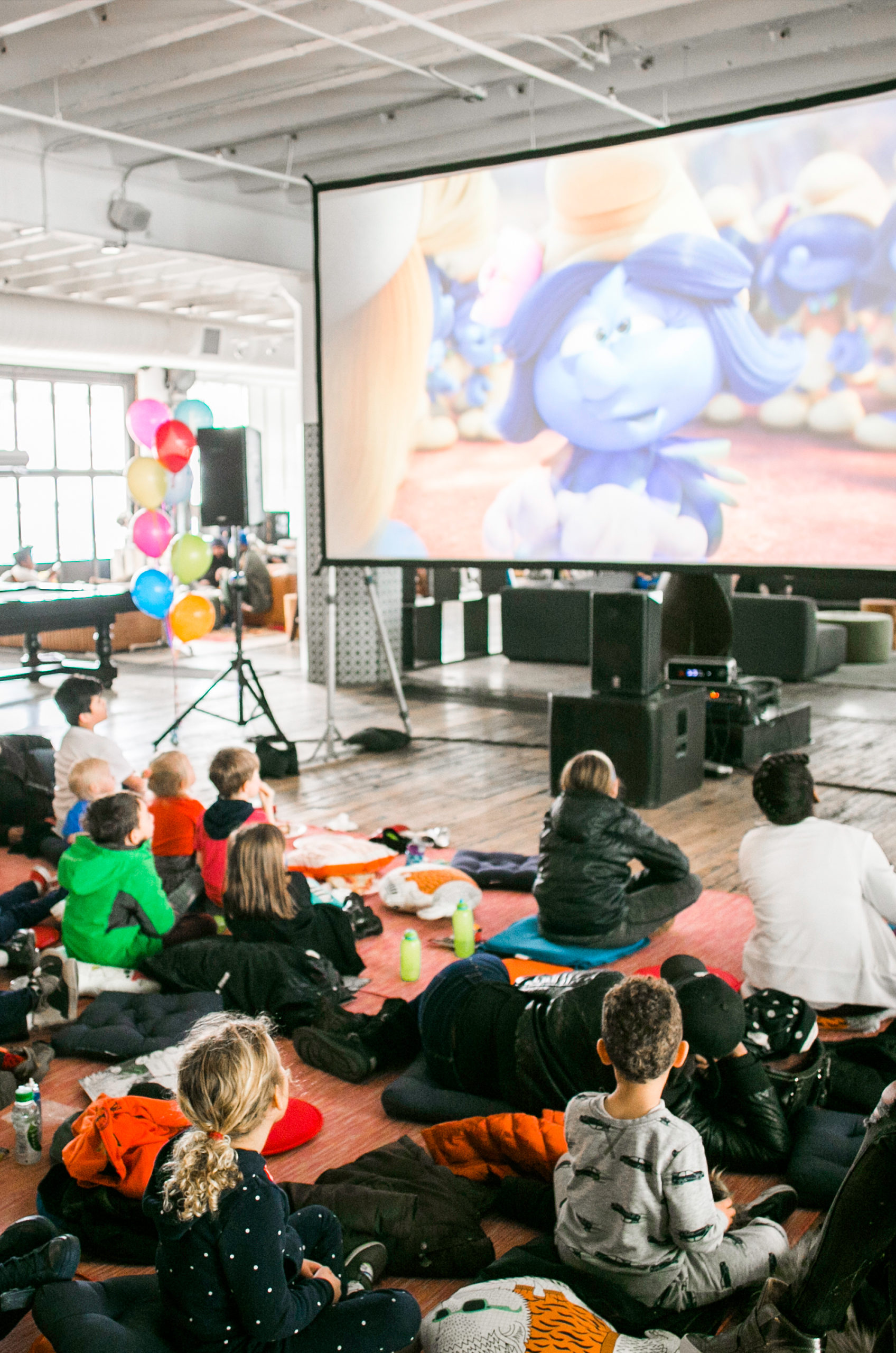 Children are sitting and watching a movie in an event space.