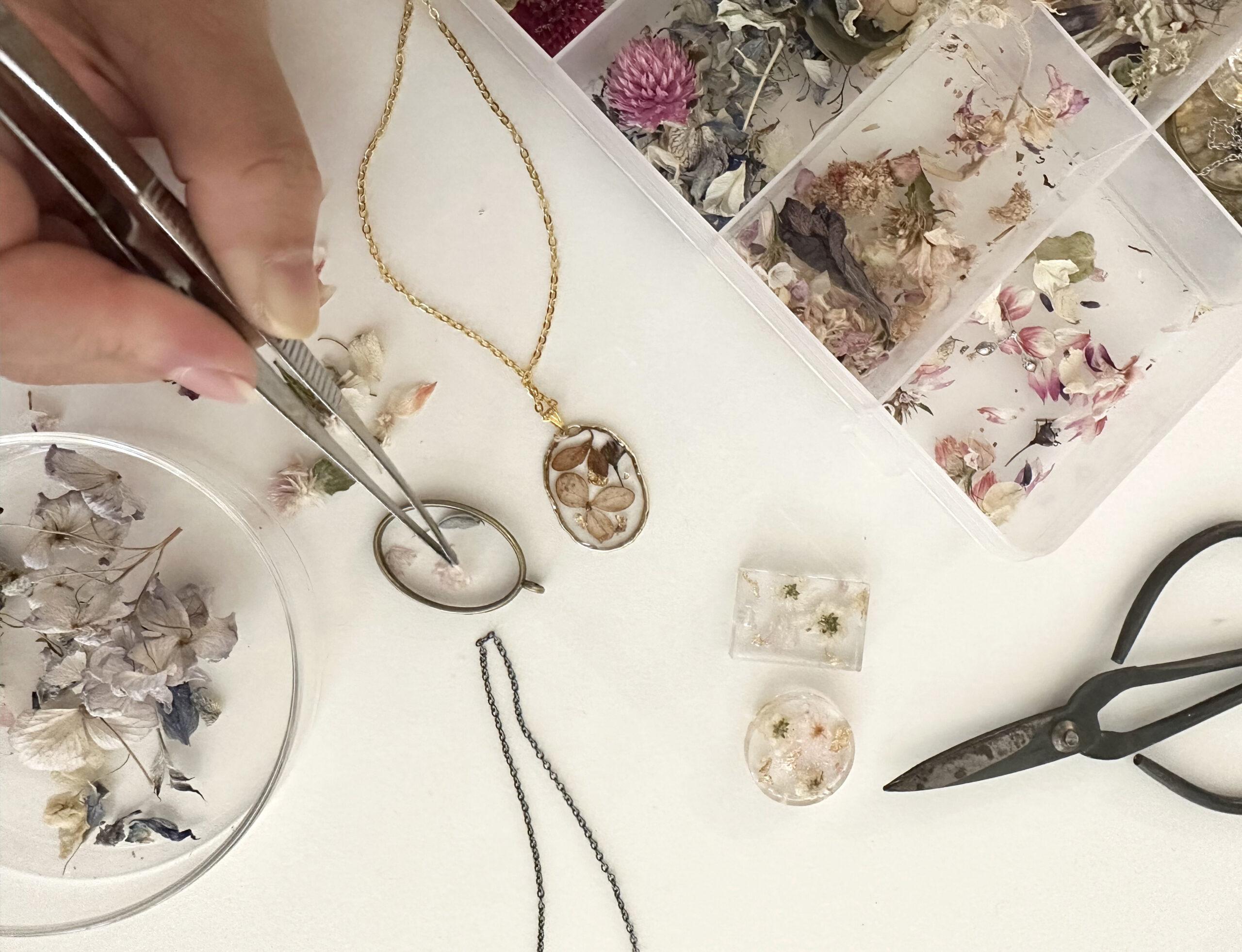 A person uses tweezers to put a dried flower in a piece of jewelry.